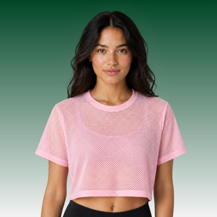 A woman modeling a light pink short-sleeve mesh crop top against a green gradient background.